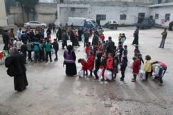 FILE - Children of Syrian families displaced from the Maaret Al-Numan region gather in the yard of a former jail turned into a makeshift refugee shelter in the northwestern city of Idlib, Dec. 31, 2019.