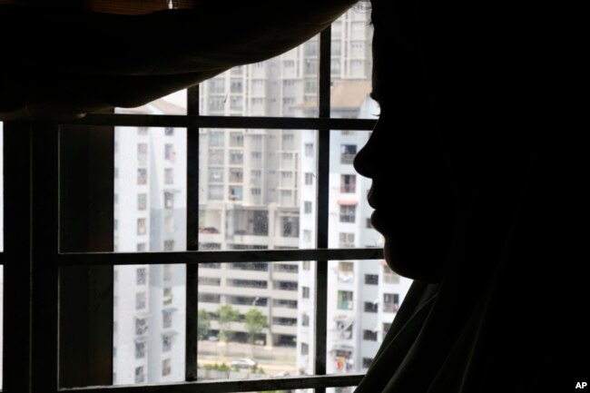 Rohingya child bride, N, age 16, stands next to a window in an apartment in Kuala Lumpur, Malaysia, on Oct. 4, 2023. An older man in Malaysia helped pay a trafficker for her passage to Malaysia in 2023 so that she could marry him. (AP Photo/Victoria Milko)