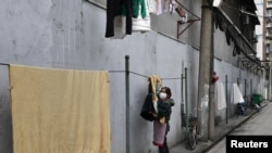 ແມ່ຍິງຄົນນຶ່ງໃສ່ຜ້າປິດປາກໄວ້ໃນຂະນະທີ່ຕາກເຄື່ອງຢູ່ຮ່ອມ ເຮືອນໃນນະຄອນວູຫານ ທີ່ເປັນບ່ອນເລີ້ມຕົ້ນຂອງການລະບາດ ຂອງໄວຣັສໂຄໂຣນາ (ພາບຖ່າຍວັນທີ 4 ມີນາ, 2020 ໂດຍ REUTERS/Stringer CHINA OUT)