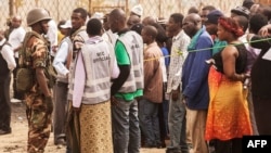 FILE - A Malawian soldier stands guard while Malawians wait in line to cast their ballots, May 21, 2014. 