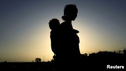 FILE - An Ethiopian woman who fled the fighting in the Tigray region carries her child near the Setit river on the Sudan-Ethiopia border in Hamdayet village in eastern Kassala state, Sudan, Nov. 22, 2020. 