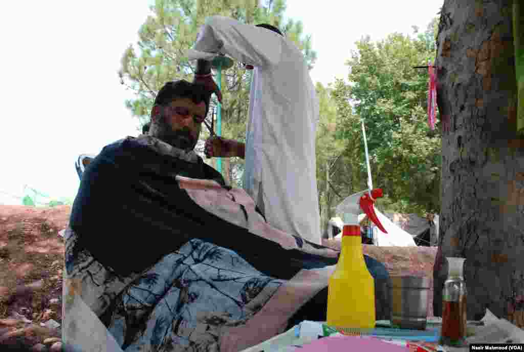 دھرنے میں شریک ایک شخص اسی احتجاج میں شامل ایک حجام سے بال کٹوا رہا ہے۔