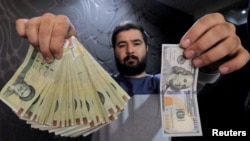 FILE - A money changer poses for the camera with a U.S hundred dollar bill (R) and the amount being given when converting it into Iranian rials (L), at a currency exchange shop in Tehran's business district, Iran, Jan. 20, 2016.