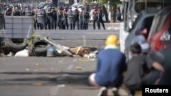 Manifestantes se refugian detrás de una barricada y algunos vehículos mientras los agentes de la policía antidisturbios se paran frente a ellos durante una protesta contra el golpe militar en Rangún, Myanmar, el 1 de marzo de 2021.