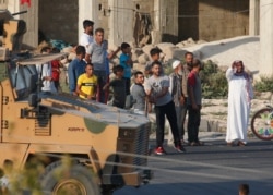 People watch as a Turkish military convoy moves near the border, shortly after the start of a Turkish operation inside Syria, through the town of Akcakale, Sanliurfa province, southeastern Turkey, at the border between Turkey and Syria, Oct. 9, 2019.