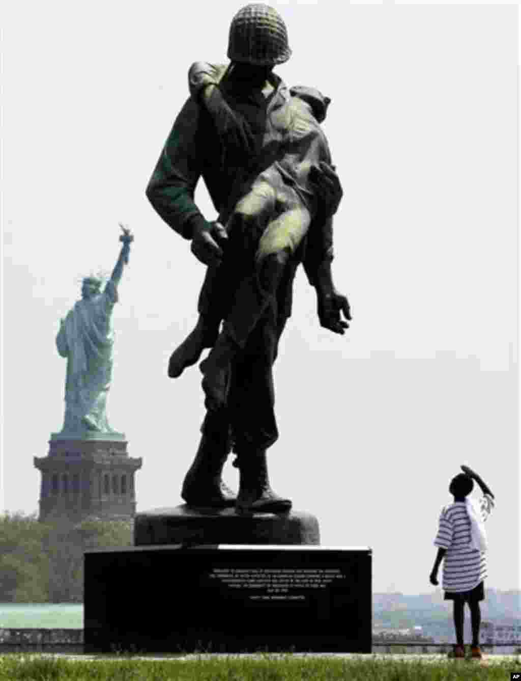 With the Statue of Liberty in the distance, Jaden Crandell, 10, salutes a statue by Natan Rapoport depicting a soldier carrying a World War II concentration camp survivor during a Memorial Day outing with his family, Monday, May 28, 2012, at Liberty State
