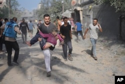 FILE - A Palestinian carries a boy wounded during the Israeli bombardment of the Gaza Strip in Deir Al-Balah, Sunday, Oct. 22, 2023.