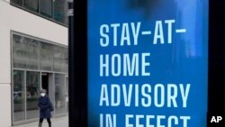 In this Nov. 18, 2020, file photo, a lone pedestrian walks past a public service sign reminding Chicago residents of the return to a stricter COVID-19 protocol along the city's usually busy Magnificent Mile in Chicago.