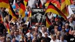 AfD supporters march with a poster showing German Chancellor Angela Merkel in Berlin, Germany, Sunday, May 27, 2018.