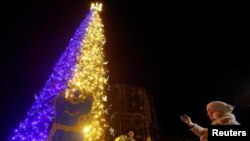 A woman sings a carol in front of a Christmas tree, amid Russia's attack on Ukraine, at the Sofiyska Square in Kyiv, Ukraine, Dec. 19, 2022. 