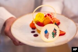 FILE—White House Executive Pastry Chef Susie Morrison holds a dessert of a white chocolate basket with banana ganache, raspberries, peaches, and candied lime zest, during a preview of the State Dinner with Kenya, Wednesday, May 22, 2024, at the White House in Washington.