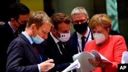 German Chancellor Angela Merkel, right, speaks with French President Emmanuel Macron, center, during a round table meeting at an EU summit in Brussels, Monday, July 20, 2020. Weary European Union leaders are expressing cautious optimism that a deal…