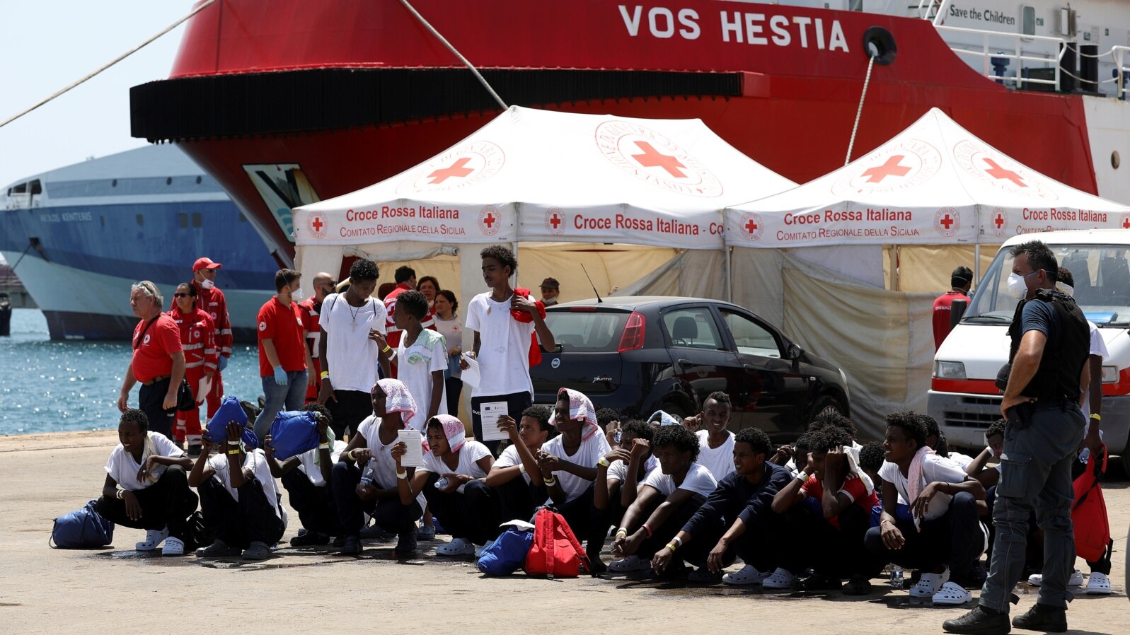 FILE - Migrants sit on the ground after disembarking from Vos Hestia ship of NGO "Save the Children" in the Sicilian harbor of Augusta, Italy, Aug. 4, 2017.