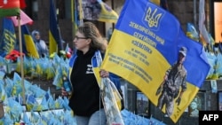 Una mujer lleva una bandera con los colores nacionales de Ucrania y el retrato de un militar ucraniano caído en un monumento improvisado en la Plaza de la Independencia en Kiev, el 2 de noviembre de 2024, en medio de la invasión rusa en Ucrania. (Foto de Sergei SUPINSKY / AFP)