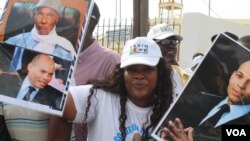 A young woman holds up pictures of Abdoulaye Wade and his son Karim as she waits for the former President at Dakar international airport, Dakar, Senegal, July 10, 2017. (S. Christensen/VOA)