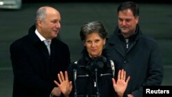 FILE - Former hostage Claudia Priest gestures after being greeted by French Foreign Minister Laurent Fabius, left, and her son upon her arrival at the Villacoublay military airport, near Paris, Jan. 25, 2015.