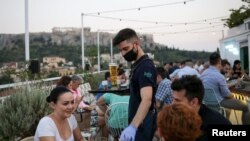 A waiter wears a protective face mask serves customers in a bar, amid the spread of the coronavirus disease (COVID-19), in Athens, Greece, Aug. 1, 2020.