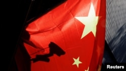 FILE — A surveillance camera is silhouetted behind a Chinese national flag in Beijing, China, Nov. 3, 2022.