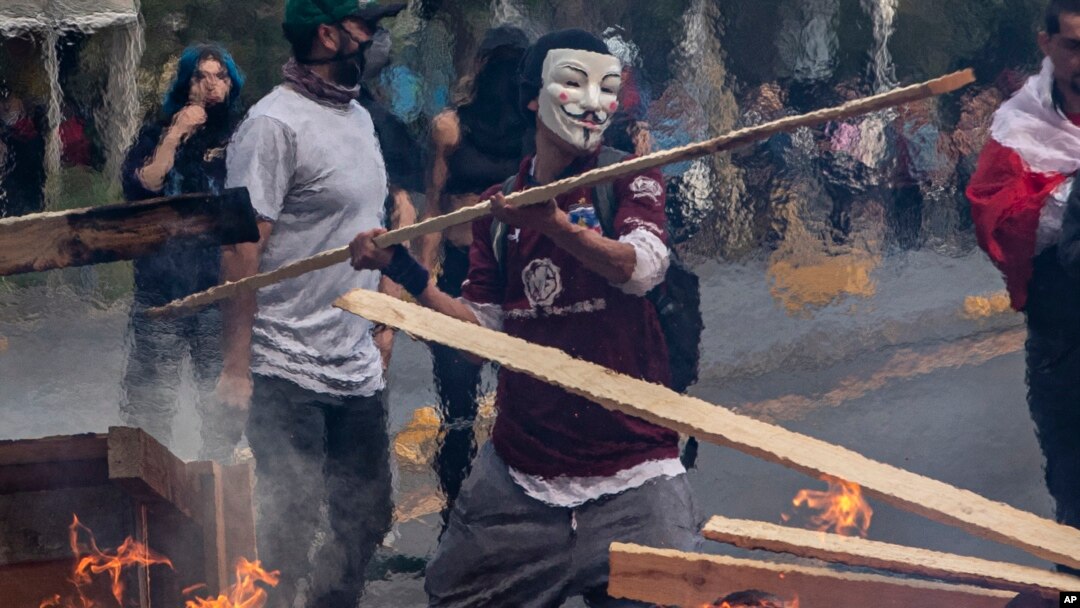 Seorang demonstran mengenakan topeng melemparkan kayu ke barikade yang dibakar dalam unjuk rasa di Santiago, Chile, 19 Oktober 2019. 