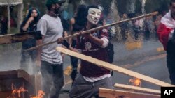 Seorang demonstran mengenakan topeng melemparkan kayu ke barikade yang dibakar dalam unjuk rasa di Santiago, Chile, 19 Oktober 2019. 