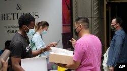 Customers, left, make returns to Saks Fifth Avenue employees at a sidewalk pickup and return desk, June 11, 2020 in New York. 