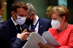 FILE - France's President Emmanuel Macron takes pictures from a document held by German Chancellor Angela Merkel during the first face-to-face EU summit since the coronavirus outbreak, in Brussels, Belgium, July 20, 2020.
