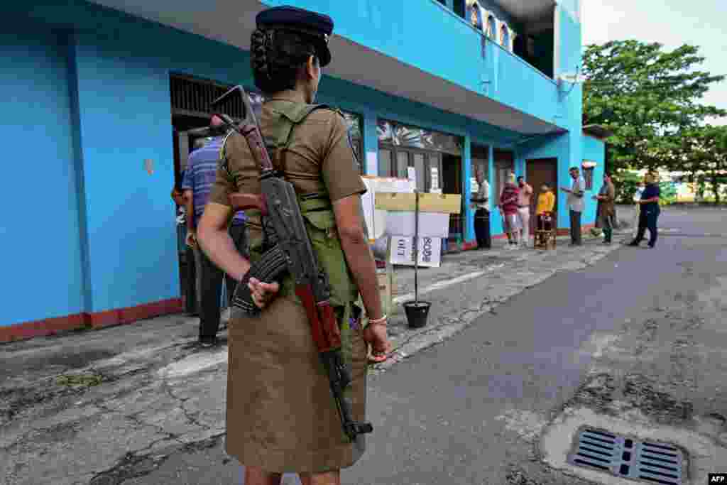 A policewoman keeps watch at a polling station as people queue before casting their ballots to vote in Sri Lanka&#39;s parliamentary election in Colombo.