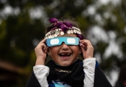 Magdalena Nahuelpan, a Mapuche Indigenous girl, looks at a total solar eclipse using special glasses in Carahue, La Araucania, Chile, Dec. 14, 2020.