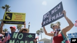 Demonstrators hold signs as they protest the lockdown and wearing masks June 27, 2020, in Huntington Beach, Calif.