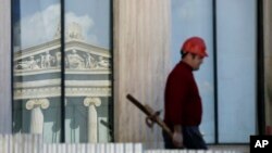 FILE - A worker carries construction material atop the 19th century Athens Academy building in central Athens, Greece.