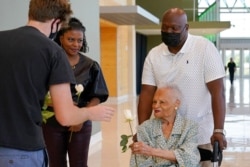 Viola Fletcher, right, the oldest living survivor of the Tulsa Race Massacre, receives a rose from Noah Lambert, left, as she arrives for a luncheon honoring survivors, May 29, 2021, in Tulsa, Okla.