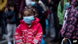 FILE - A young girl wearing a mask to prevent the spread of the coronavirus, looks on after refugees and migrants arrived at the port of Piraeus, near Athens, May 4, 2020. 