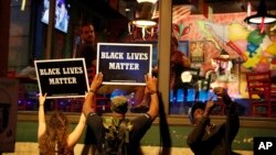 FILE - Protesters hold up signs as restaurant patrons look out the window in St. Louis, Missouri, Sept. 15, 2017.