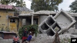 People sit outside a house that was destroyed by the January 2010 earthquake in Port-au-Prince, January 3, 2012.