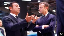 French President Emmanuel Macron listens to Carlos Ghosn, the CEO of French car maker Renault, left, at the Renault stand during an official visit at the Paris Motor Show, in Paris, France, Oct. 3, 2018.