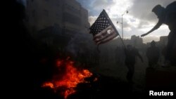 A Palestinian protester prepares to burn a U.S. flag during clashes with Israeli troops at a protest against U.S. President Donald Trump's decision to recognize Jerusalem as the capital of Israel, near the Jewish settlement of Beit El, near the West Bank city of Ramallah Dec. 7, 2017. 