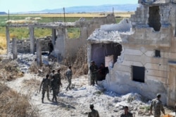 FILE - Syrian regime forces gather near a damaged building at the entrance of the town Kafr Nabuda, in the north of the Syrian Hama province, May 26, 2019.