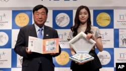 FILE - Former South Korean Olympic figure skating champion Yuna Kim, right, an honorary ambassador for the 2018 Pyeongchang Winter Olympics, and Lee hee-beom, president of the Pyeongchang Organizing Committee for the 2018 Olympic and Paralympic games, hold commemorative coins and bank notes for the 2018 Winter Olympics during the launching ceremony in Seoul, South Korea, Sept. 1, 2017. 