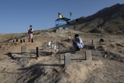 FILE - Men pray near the graves of relatives killed in May bombings, at a cemetery on the outskirts of Kabul, Afghanistan, June 2, 2021.