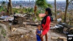 Alona Nacua berdiri di samping putranya saat melihat rumah mereka yang rusak akibat Topan Rai di kota Cebu, Filipina, pada Hari Natal, 25 Desember 2021. (Foto: AP)