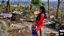 Alona Nacua stands beside her son as she looks at their damaged house due to Typhoon Rai in Cebu city, Philippines, on Christmas Day, Dec. 25, 2021.