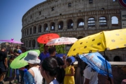 FILE - Tourists hold umbrellas to shelter from the sun during a heat wave as they walk past the Colosseum, in Rome, July 26, 2019.