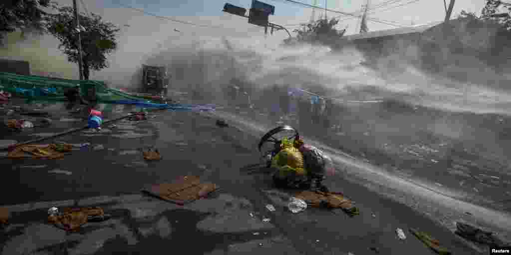 Anti-government protesters use fans to blow away tear gas as riot police use a water cannon during clashes in Bangkok, Dec. 2, 2013.