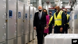 Presiden Joe Biden berjalan melewati lemari es yang digunakan untuk menyimpan vaksin COVID-19 Pfizer-BioNtech saat dia mengunjungi lokasi manufaktur Pfizer, Jumat, 19 Februari 2021, di Portage, Michigan. (Foto: AP/Evan Vucci)