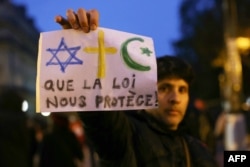 A protester, showing a placard which reads as "May law protect us" and depicting a Star of David (L), a Christian cross and a Turkish crescent and a star, takes part in a march against anti-Semitism in Paris on November 12, 2023.
