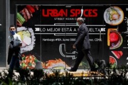 People wearing face masks walk past a sign advertising a restaurant in Mexico City, June 5, 2020.