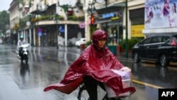 FILE - A woman in a poncho rides a bicycle during heavy rainfall in Hanoi, Oct. 14, 2020, as tropical storm Nangka made landfall in north-central Vietnam. 