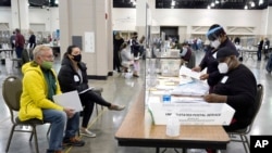 Trabajadores electorales (der.) verifican votos bajo la mirada de observadores (izq.) durante el reconteo a mano de votos presidenciales en el Centro Wisconsin, en Milwaukee, el viernes 20 de noviembre de 2020.