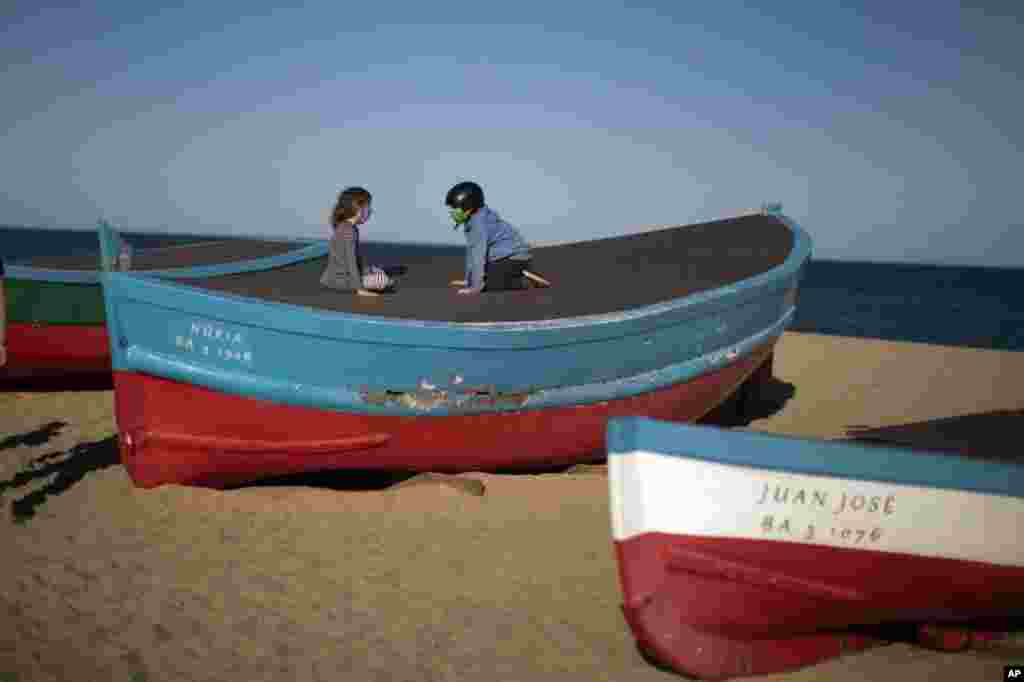 Children wearing face masks sit on top of a boat in a beach in Badalona, near Barcelona, Spain, April 28, 2020 as the lockdown to combat the spread of coronavirus continues. 