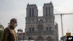 FILE - A man wears a mask to protect against the spread of the coronavirus as he walks past the Notre Dame cathedral in Paris, April 13, 2020. 